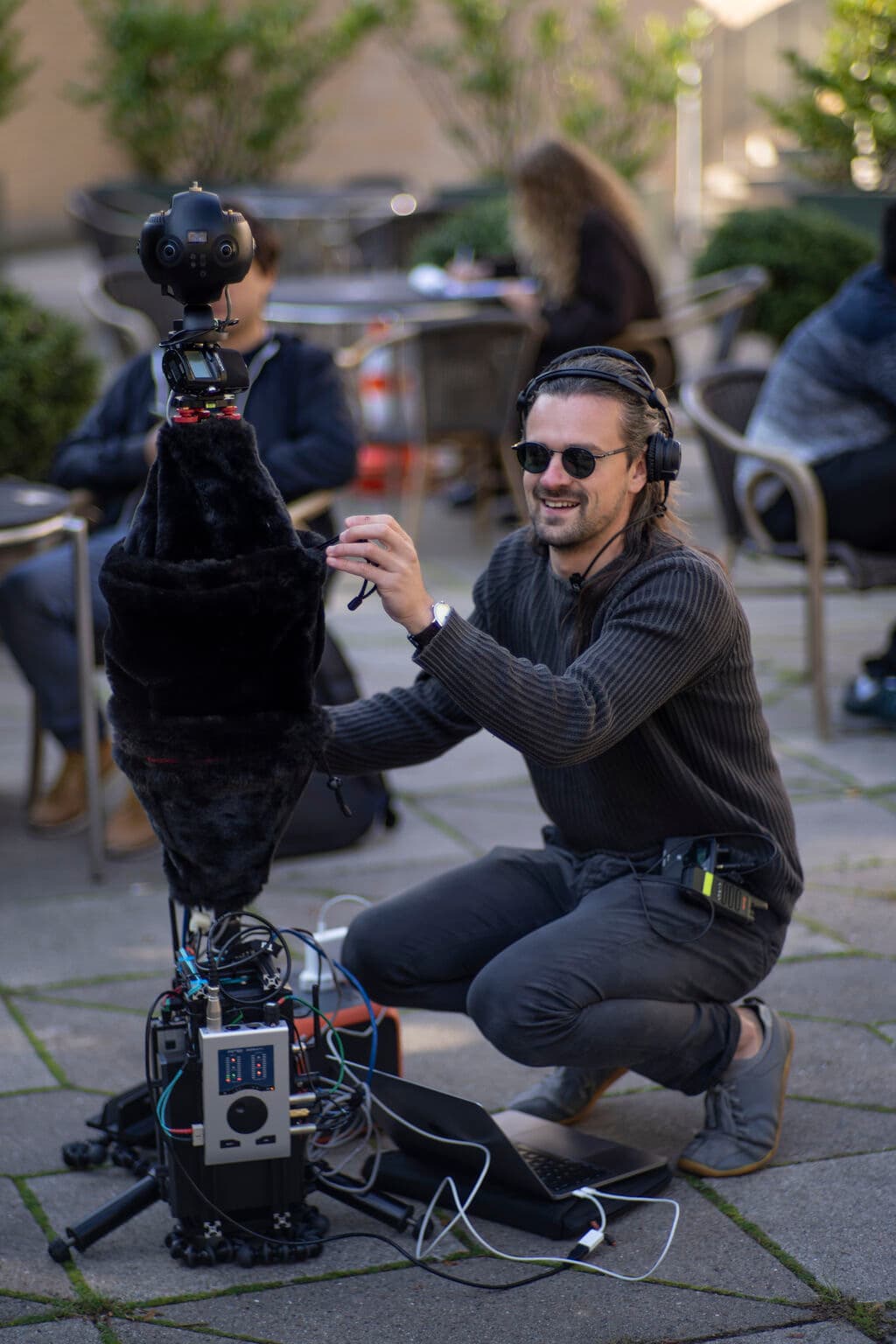 Axel Drioli in headphones, crouched beside a 360° camera and spherical microphone rig, recording outdoors